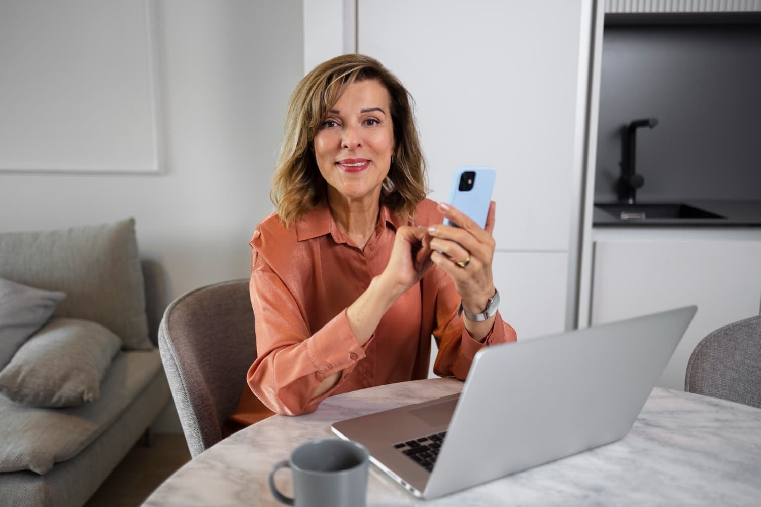 Mulher sorridente usa computador e celular para acompanhar leilões online